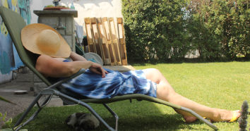 Frau mit Strohhut über dem Gesicht ruht auf einer Gartenliege im eigenen Garten hinter dem Haus